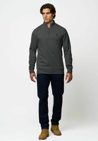 Pulover cu fermoar la gât de culoare gri închis, cu mâneci lungi, manșete și tiv cu danteluri. Asortat cu blugi negri și bocanci deschiși la culoare cu șireturi.