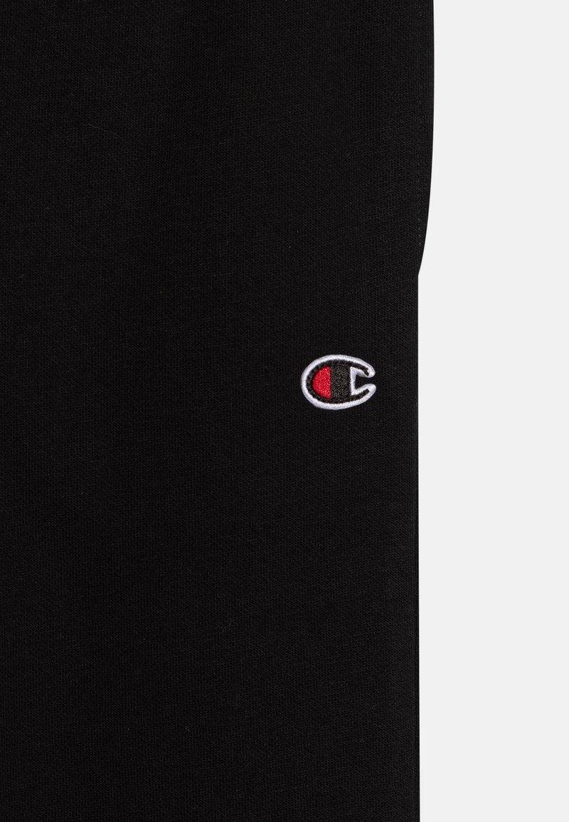 Un tissu en coton noir présente un logo brodé avec un design circulaire en blanc, rouge et noir, placé sur le côté inférieur droit.