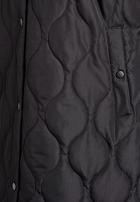 Melna vējjakas veste ar viļņu rakstu, sprādzēm un sānu kabatu. Izgatavota no gludas auduma ar matētu virsmu.