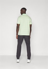 Polo shirt vert clair avec un motif en zigzag texturé, associé à un pantalon sombre et des baskets blanches. Manches courtes et design de col.