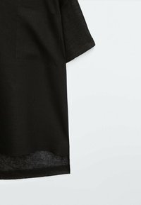 Maglietta nera a maniche corte realizzata in tessuto leggero. Presenta una tasca frontale e un orlo leggermente trasparente. Design semplice con vestibilità comoda.