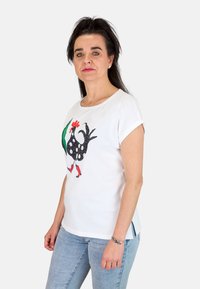 Camiseta blanca de manga corta con un gráfico de gallo moteado en blanco y negro con acentos rojos. Tela suave, corte relajado.