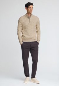 Beige kabelstickad tröja med halv dragkedja, kombinerad med mörka byxor och ljusa sneakers. Texturerad tyg med en avslappnad passform.