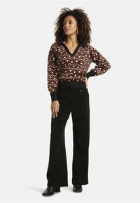 Brown patterned knit sweater with a V-neck and black collar, paired with black corduroy flared pants and black heeled boots.