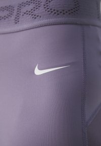 Fialové sportovní legíny s texturovaným pasem a bílým logem Nike. Mají hladký materiál a pohodlný střih s vyztuženým švem.