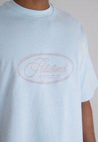 Light blue cotton T-shirt featuring a round neckline and a central embroidered design with the word "Prohibited" and five stars below.