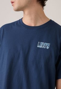 Μπλε ναυτικό βαμβακερό μπλουζάκι με στρογγυλή λαιμόκοψη και κοντά μανίκια, που φέρει μπλε κεντημένο λογότυπο "LEVI'S" στο αριστερό μέρος του στήθους.