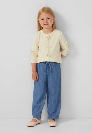Cremefarbenes, geripptes Langarmoberteil mit dekorativen Schleifen, kombiniert mit lockeren blauen Jeans und beigen Schuhen. Einfaches und lässiges Outfit-Design.