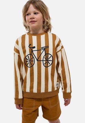 Enfant aux cheveux blonds mi-longs portant un pull à rayures verticales marron et crème avec un motif de bicyclette noire et un short marron.