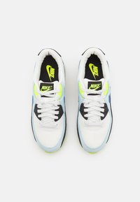 Adidașii Nike au un upper din plasă albă cu accente albastre și negre, detalii verde neon și o limbă neagră cu un logo Nike galben.