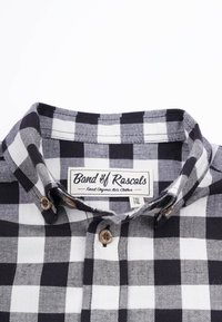 Svartvit rutigt flanellskjorta med krage, prydd med bruna knappar och en etikett som säger "Band of Rascals" vid halsen.