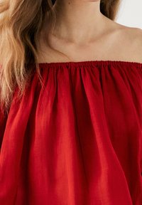 Rød off-the-shoulder bluse med samlet hals, letvægtsstof og flydende tekstur. Udsmykket med bløde plisseringer og en afslappet pasform.