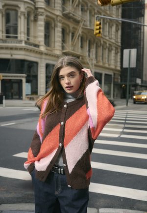 Multicolored cardigan featuring diagonal orange, pink, and brown patterns, with button detailing and a soft, textured fabric.