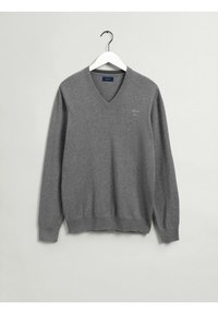 Pull gris col en V en tissu doux avec manches longues. Comprend des poignets et un ourlet côtelés, avec un petit logo sur le côté gauche de la poitrine.