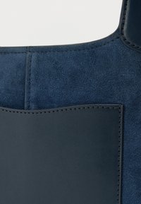 Τσάντα tote από σουέτ σε ναυτικό μπλε, με λεπτομέρειες από λείο δέρμα, δομημένο σχήμα και ραφές σε ίδιους τόνους κατά μήκος των άκρων.