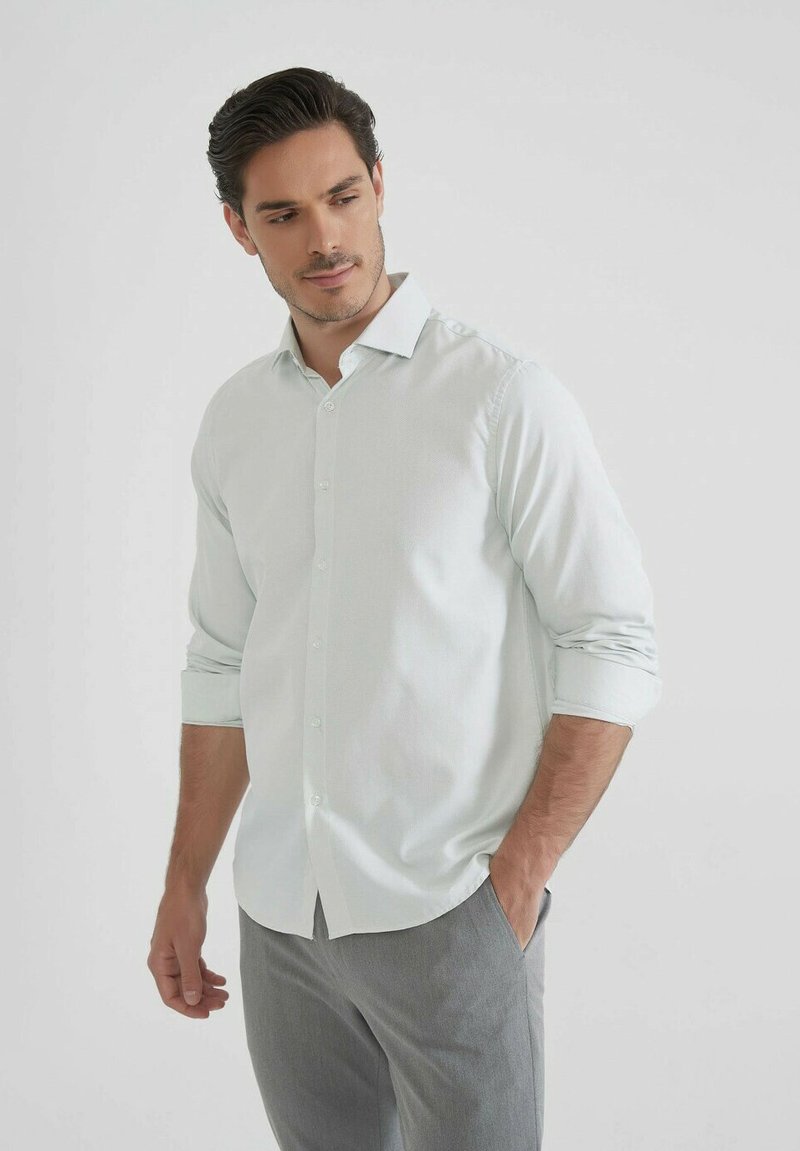 Chemise à manches longues bleu clair avec un col boutonné, boutons à l'avant et poignets retroussés, assortie à un pantalon gris, texture de tissu lisse.