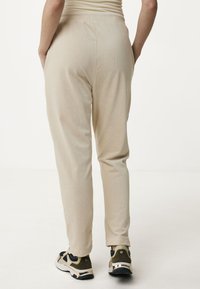 Beige elastische taillebandbroeken met een ontspannen pasvorm, voorzien van een zachte textuur en zijzakken, in combinatie met zwarte en olijfgroene sneakers.