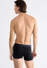 Boxer shorts neri in cotone con una texture liscia, dotati di un elastico scuro in vita. La visuale mostra il retro dei pantaloni e un torso nudo.