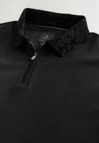 Pullover negro con media cremallera y cuello negro estampado, que presenta un tejido de textura suave y detalles de cremallera metálica. Etiqueta de la marca visible en el interior.
