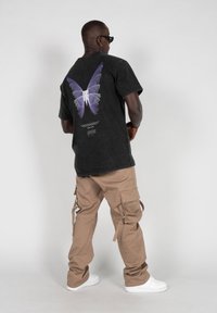 Black oversized t-shirt with purple butterfly graphic on the back, paired with khaki cargo pants and white sneakers.