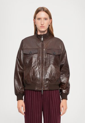 Veste aviateur en cuir marron avec un col haut, deux poches poitrine et des poignets côtelés. Texture lisse avec une finition brillante et fermeture éclair.