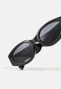 Sorte solbriller med et dristigt, vinklet design, der har overdimensionerede tonede linser og en blank finish. Accenter inkluderer en fremtrædende rammeform.