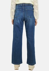 Pantalones vaqueros de pierna ancha en denim azul medio, con una cinturilla texturizada, dos bolsillos traseros y un corte recto desde la cadera hasta el dobladillo.