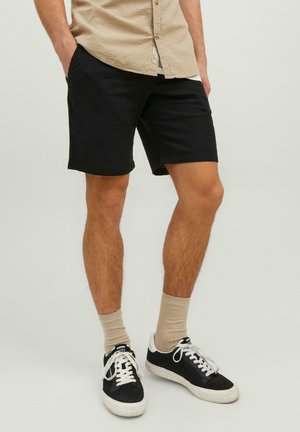 Schwarze Shorts aus leichtem Material, mit geradem Schnitt, kombiniert mit beigen Socken und schwarzen Sneakers mit weißen Akzenten.
