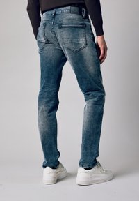 Niebieskie dżinsy z denimu z efektem sprania, o prostych nogawkach, tylnych kieszeniach i detalem z metką na pasku. Połączone z białymi trampkami.