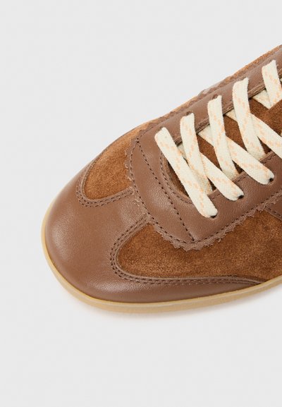 Bruna läder- och mockasneakers med texturerad yta, krämfärgade snören och subtila sömnadsdetaljer. Rundad tå och sula av gummigummi.