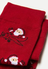 Röda stickade strumpor som har en design av jultomten i ett flygplan. Texturen är ribbad med svarta och vita detaljer för grafiken.