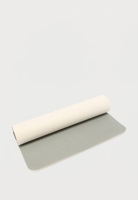 Στρώμα γιόγκα με υφή ελαφρώς γκρι επιφάνειας, τυλιγμένο μερικώς με λείο κρεμ χρώμα στην κορυφή. Οι άκρες είναι στρογγυλεμένες· το στρώμα είναι ευλύγιστο και ελαφρύ.