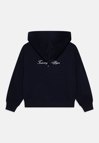 Navy blå hettegenser med snor i hetten, ribbestrikkede mansjetter og brodert "Tommy Hilfiger"-logo på baksiden. Laget av myk bomullsblanding.