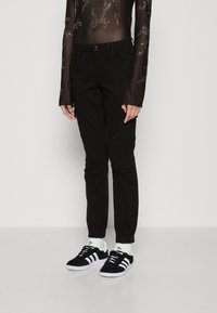 Μαύροι tapered jogger παντελονιού με ελαστικά μανίκια, διαθέτοντας πλαϊνές τσέπες. Συνδυασμένοι με μαύρα σουέτ αθλητικά παπούτσια και λευκές κάλτσες. 