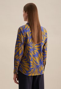 Camicia a maniche lunghe in tessuto blu con motivo a foglie gialle, con vestibilità ampia, polsino con bottone e dettaglio della yoke sul retro.