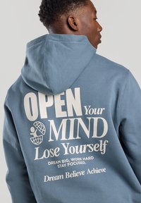 Blue hoodie with a drawstring and textured fabric. It features large white text on the back with motivational phrases and graphics.