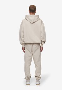Sudadera y pantalones jogger de algodón beige, con un ajuste relajado, puños acanalados y capucha con cordón. El calzado es blanco con suelas texturizadas.