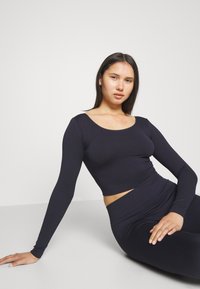 Marinblå ribbad långärmad topp med rundad halsringning, parat med matchande ribbade högmidjade leggings. Slät textur, figurnära design.
