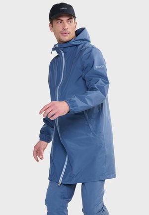 Giacca impermeabile blu con zip completa, cappuccio e polsini elasticizzati; presenta tasche laterali e il logo "Aigle" sulla manica.