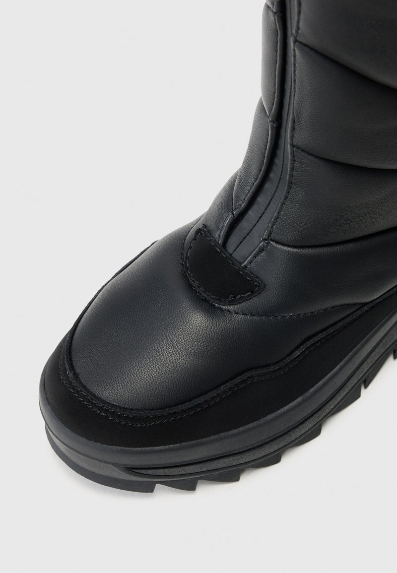 Schwarze gepolsterte Stiefel mit einem glatten Lederobermaterial, Gummisohle mit Traktionsrillen und einem Reißverschluss an der Seite.