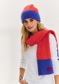 Zestaw czapka i szalik w kolorach różowym i niebieskim. Czapka posiada prążkowany wzór; szalik jest długi, z kontrastowymi sekcjami i zawiera metkę z marką.