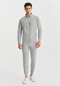 Szara bluza na zamek i dopasowane spodnie dresowe z miękkiego materiału, z przylegającym krojem i ściągaczami przy mankietach, zestawione z białymi trampkami.