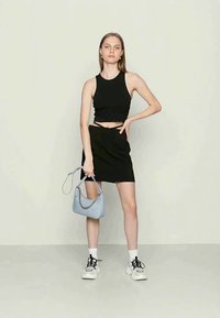 Top cropped preto e saia justa preta, combinados com meias brancas e ténis chunky. Bolsa azul clara com detalhes em corrente.