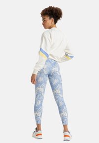 Felpa bianca con strisce blu e gialle, abbinata a leggings azzurri chiari con un motivo di ananas e foglie.