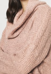 Hellrosa gestrickter Pullover mit weitem Rollkragen. Verfügt über ein strukturiertes Muster und gerippte Bündchen. Weiches, gemütliches Material mit lässiger Passform.