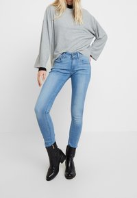 Jeans ajustados de color azul claro con cintura alta, combinados con una blusa de manga larga gris. Botines negros de tobillo con cremallera lateral completan el atuendo.