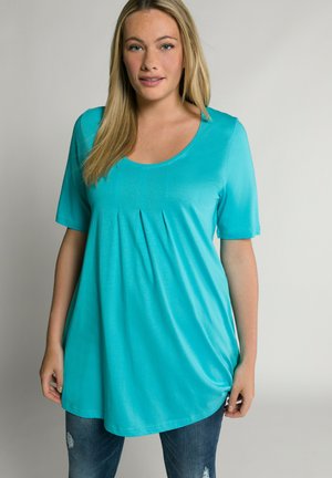 Top turchese a maniche corte con scollatura a girocollo e pieghe sul davanti, realizzato in un tessuto leggero e liscio, abbinato a jeans strappati.