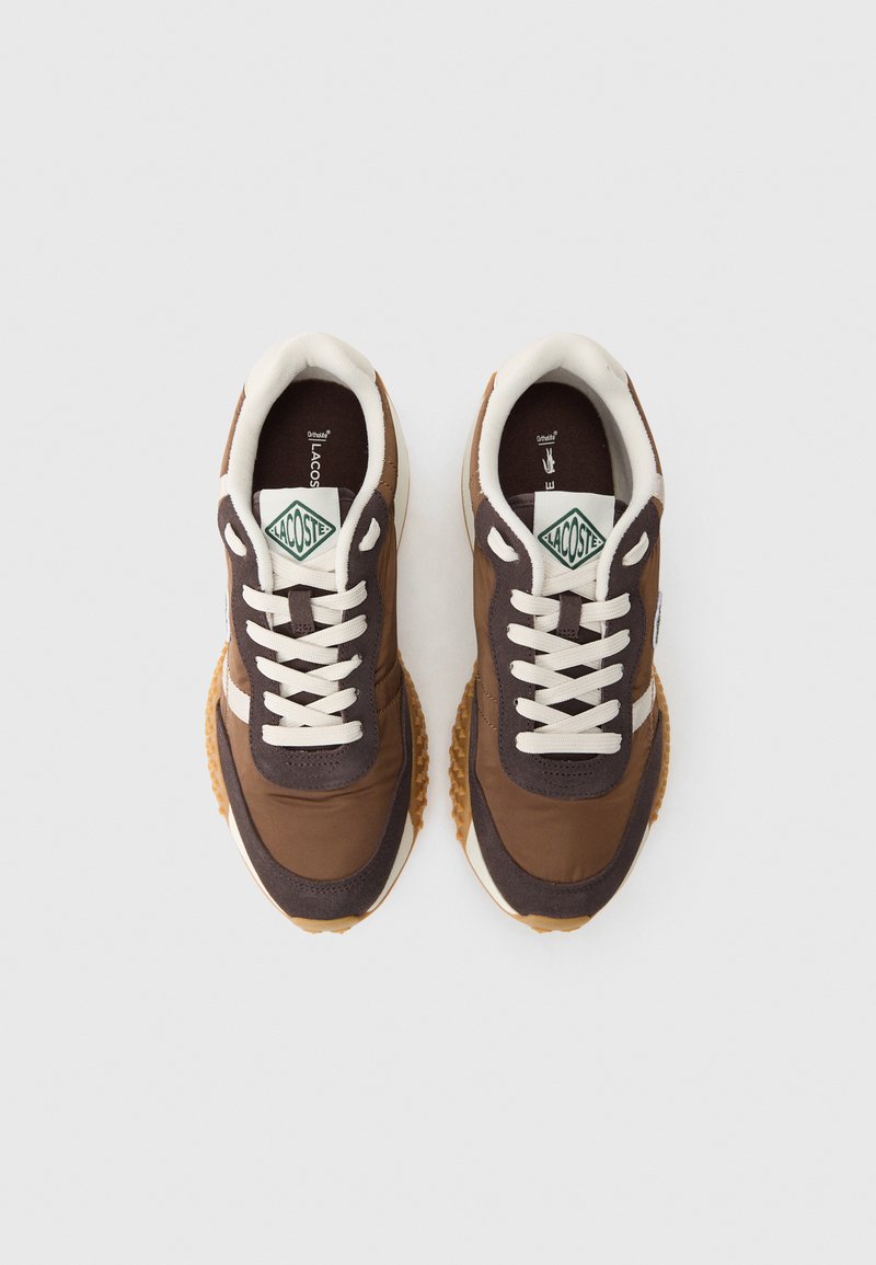 Zapatillas deportivas marrones con acentos en beige, cordones blancos y suela texturizada. Presenta un parche de logo verde y blanco en la lengüeta.