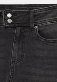 Sort denim jeans tæt på, der viser linningen, bæltestrop, forlomme og to sølvknapper ved lynlåsområdet.