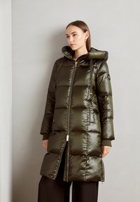 Olive zelený prešívaný kabát s kapucňou, so zipsom vpredu, prešívaným dizajnom, elastickými manžetami a bočnými vreckami. Hladký, lesklý povrch.